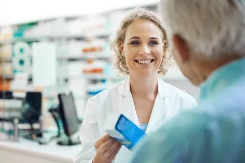 A pharmacist handing a senior a box of medication.