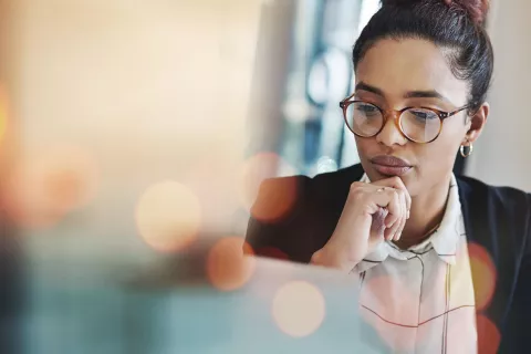 Young adult with glasses staring at a laptop.