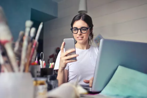 Young adult holding phone while at a desk.