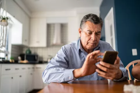 Adult at the kitchen table, looking at a cell phone.