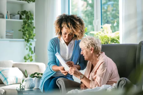 An adult reviewing paperwork with a senior on the couch.