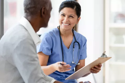 A doctor smiling at a senior while holding a clipboard.