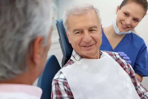 A senior adult at the dental office with the dentist, and dental assistant.