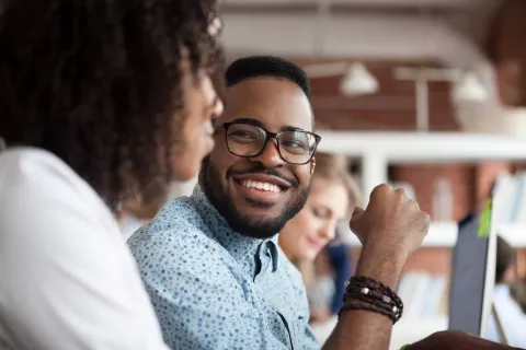 Adult smiling while at the desk with coworkers.