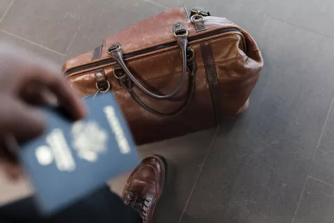 Hand holding passport and luggage on the ground.