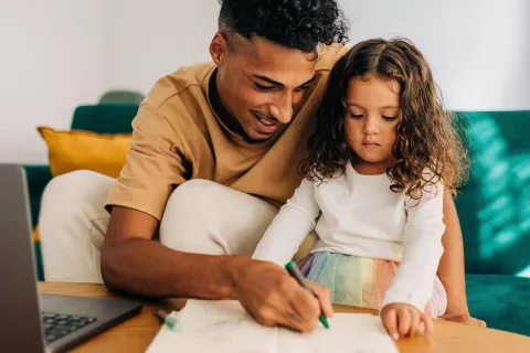 An adult and child coloring on a piece of paper together.