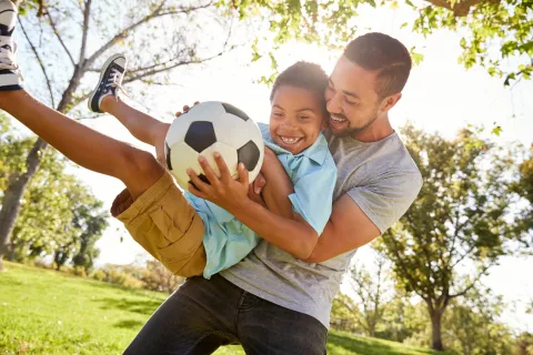 Adult playing with a child holding a soccer ball.