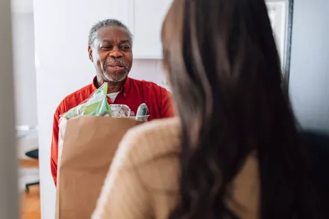 A person delivering groceries to a senior.