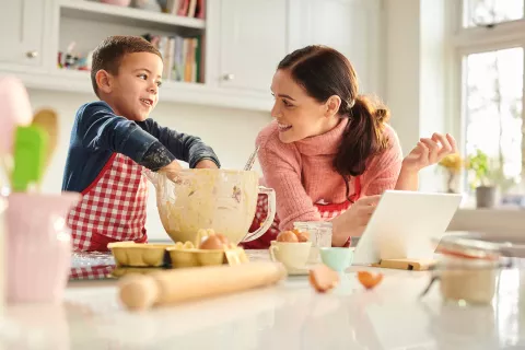 A child mixing batter with their hands while with an adult.