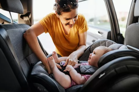 An adult buckling a baby into their car seat.