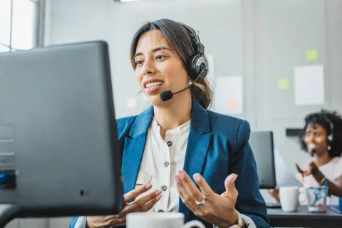 Adult with a headset speaking with someone while on the computer.