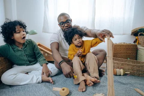 an adult and two children playing with wooden toys on the floor