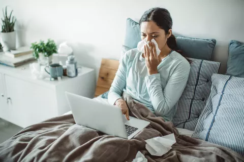 Adult in bed with a tissue while using the laptop.