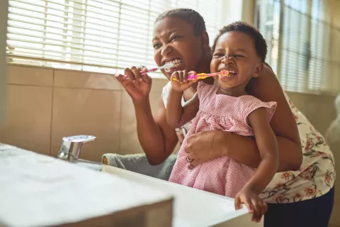 An adult and a child brushing their teeth.