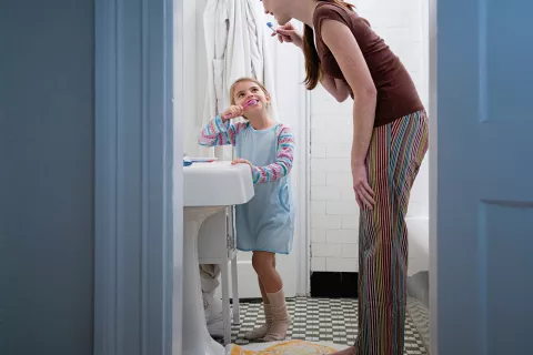 adult and child in a bathroom, brushing their teeth.