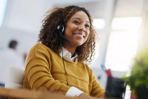 A young adult with a headset on smiling at the computer.