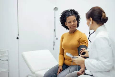 Adult sitting on the medical chair while getting their blood pressure taken by a doctor.