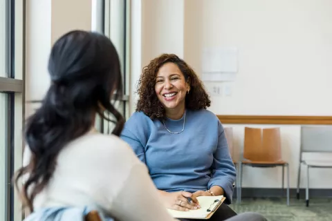 Two adults speaking to each other while sitting down.