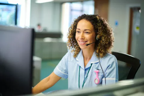 Nurse smiling at the computer with a headset on.