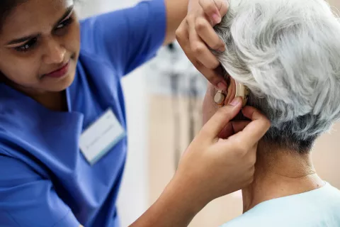 A doctor adjusting a senior person's hearing aid.