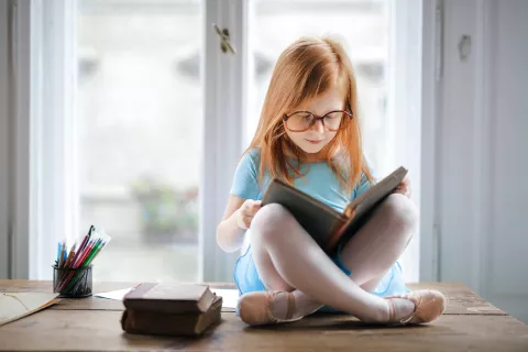 A child reading a book while sitting on top of a table.