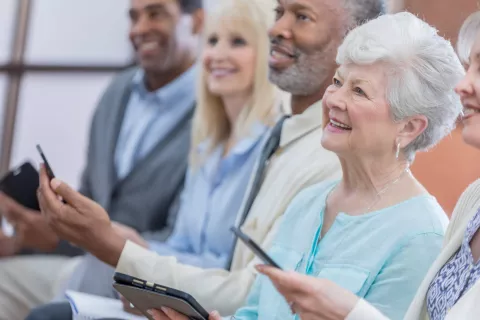 A group of seniors holding digital devices and smiling.