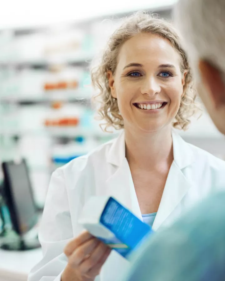 A pharmacist handing a senior a box of medication.