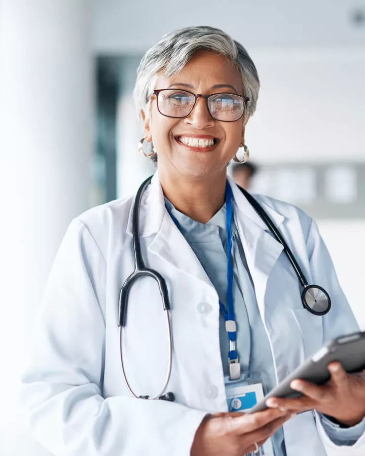 A doctor smiling while holding a digital tablet.