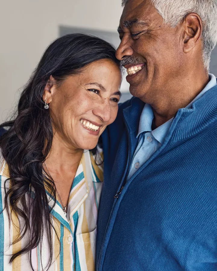 Two senior adults embracing each other with smiles.