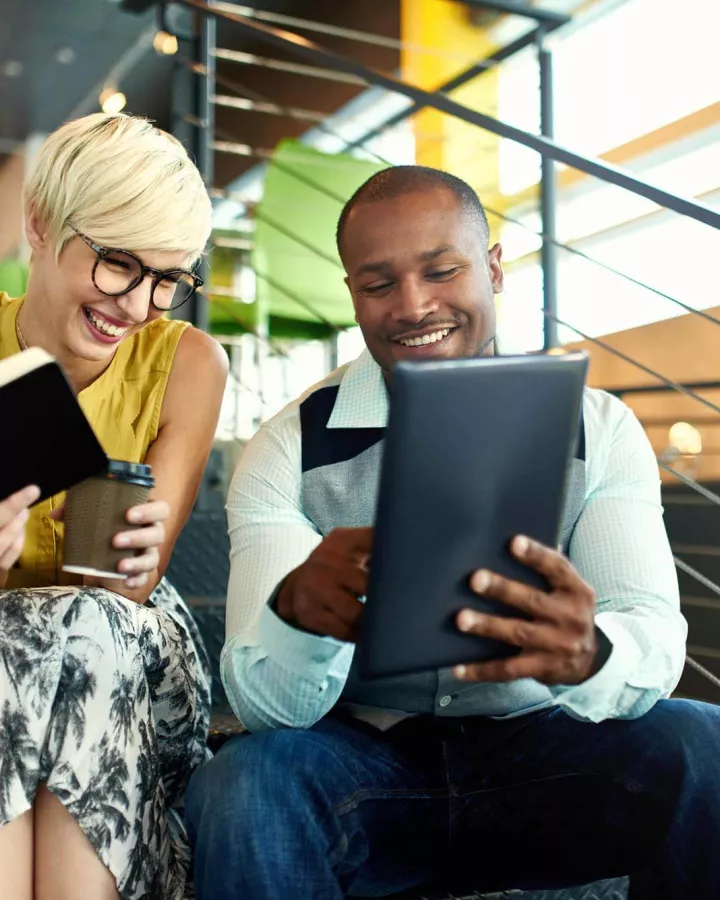 Adults sitting next to each other on the stairs while looking at a digital tablet.