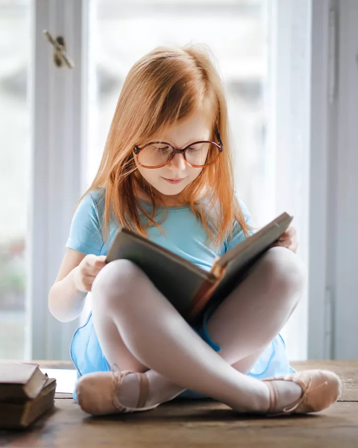 A child reading a book while sitting on top of a table.